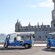 Two 3-wheeled motorized vehicles parked outside a historical building by the sea